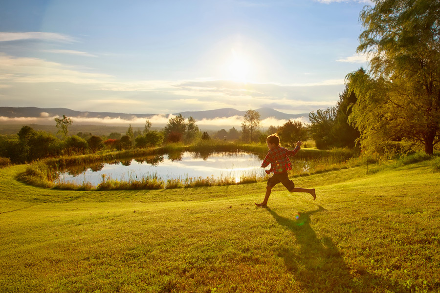 Boy running outside in front a small pond in Vermont